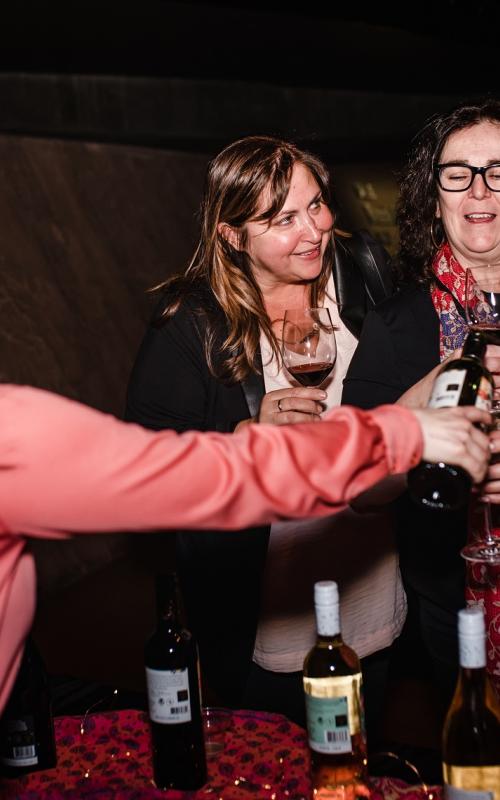 Four femme-presenting folks cheering over a bottle of wine