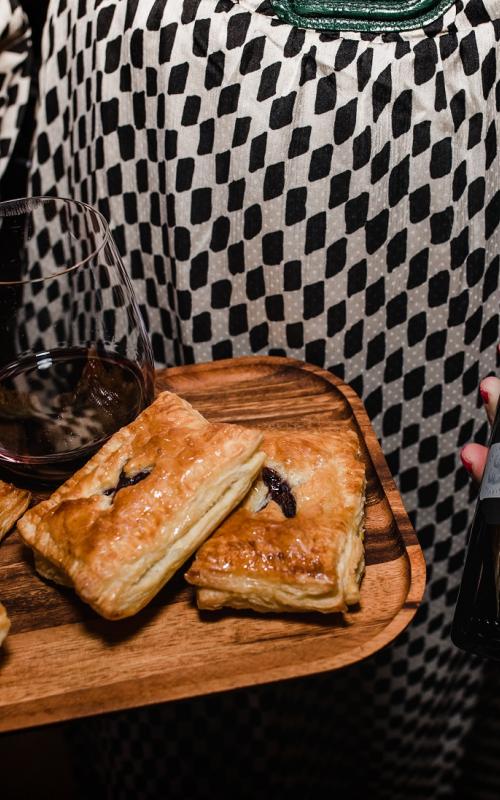 Woman holding tray of appetizers and bottle of wine.